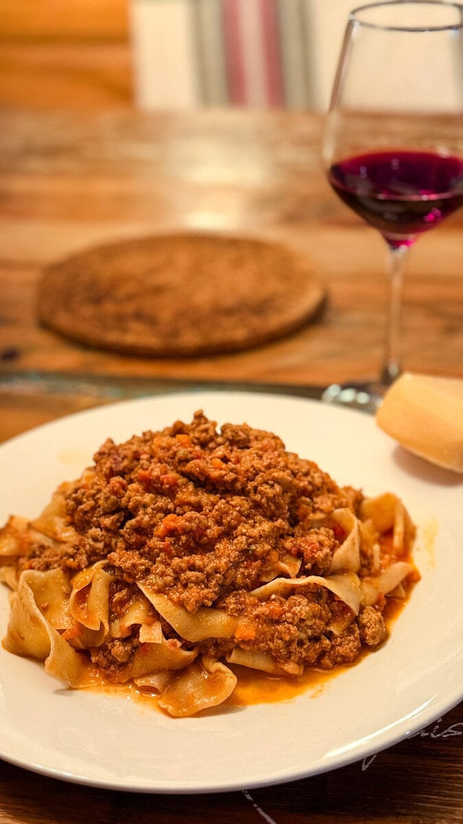 bol de papardelle en sauce bolognaise sur table en bois avec coupe de vin et blog de fromage parmesan