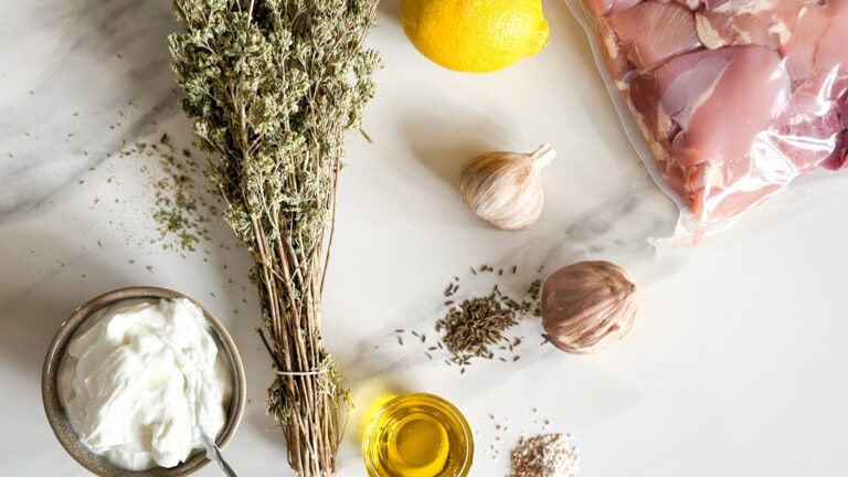 yogourt, bouquet d'origan sec, tête d'ail, citron, huile, épice et haut de cuisse de poulet sur comptoir blanc