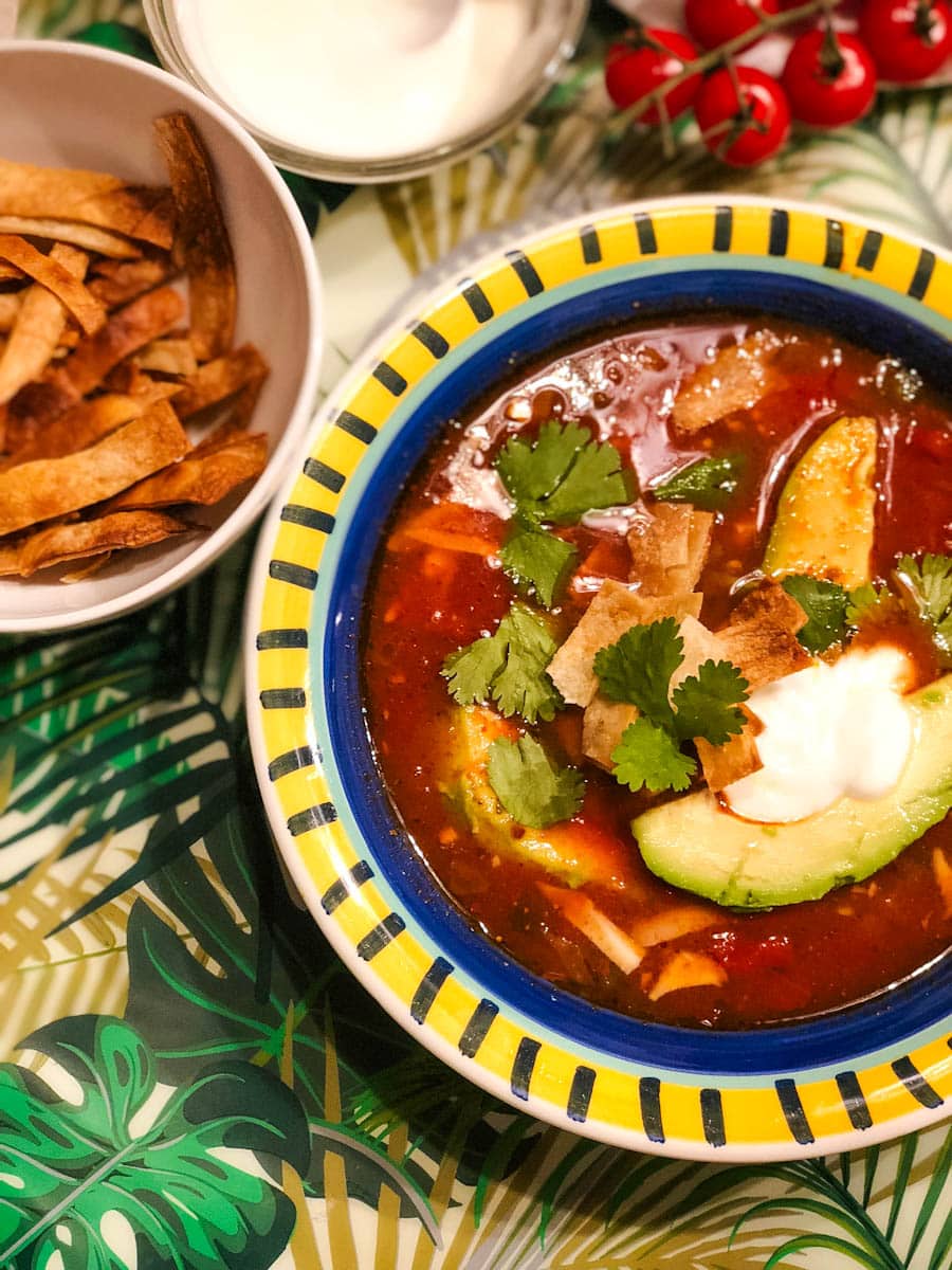 soupe aux tortillas dans un bol coloré avec garnitures: crème sûre, tortilla, coriandre et bol de tortilla en lanière frite