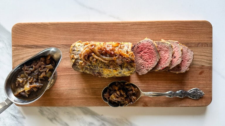roti sur une planche avec garniture d'oignons caramélisés dans une cuillère et sauce dans une saucière