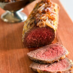 rôti français avec tranches rosées et oignons caramélisés sur une planche en bois