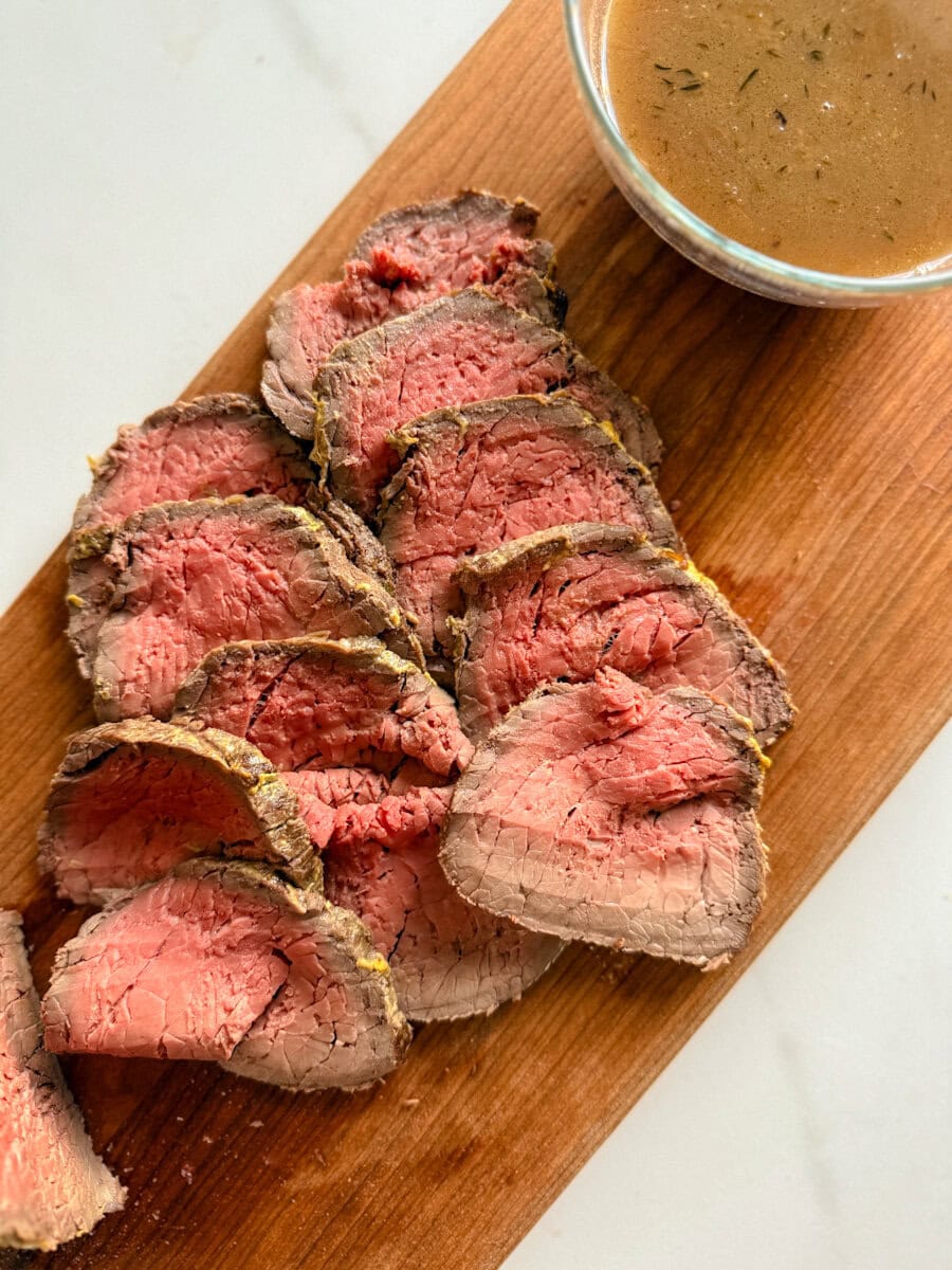 tranches de roti de boeuf sun une planche de bois avec bol de sauce 