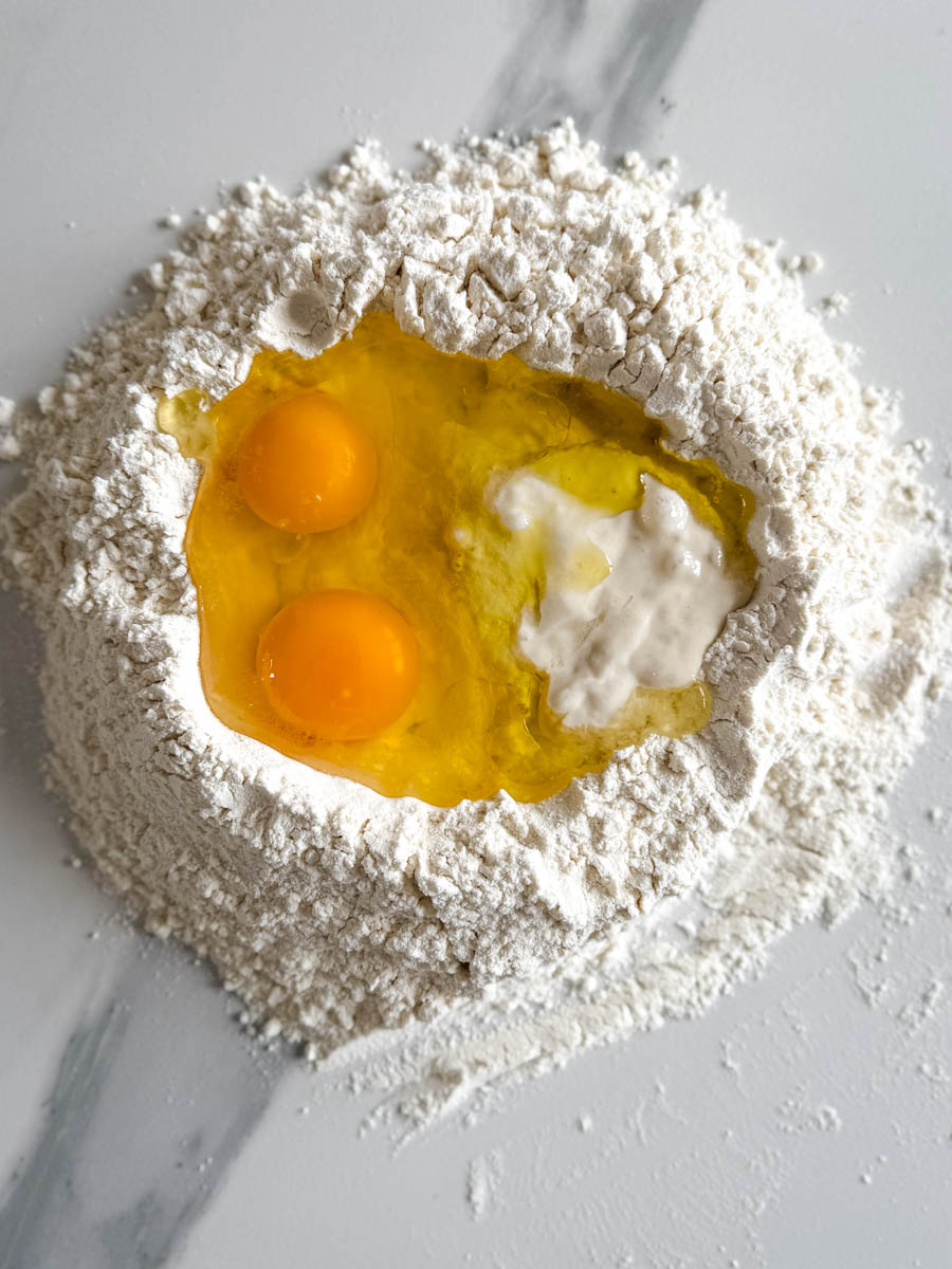 nid de farine avec oeufs, levain et huile d'olive à l'intérieur sur comptoir blanc