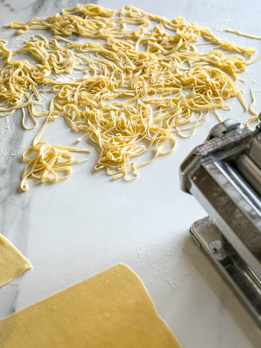 pâtes fraiches aux oeufs, machine à pâte manuelle et pâte sur un comptoir blanc 