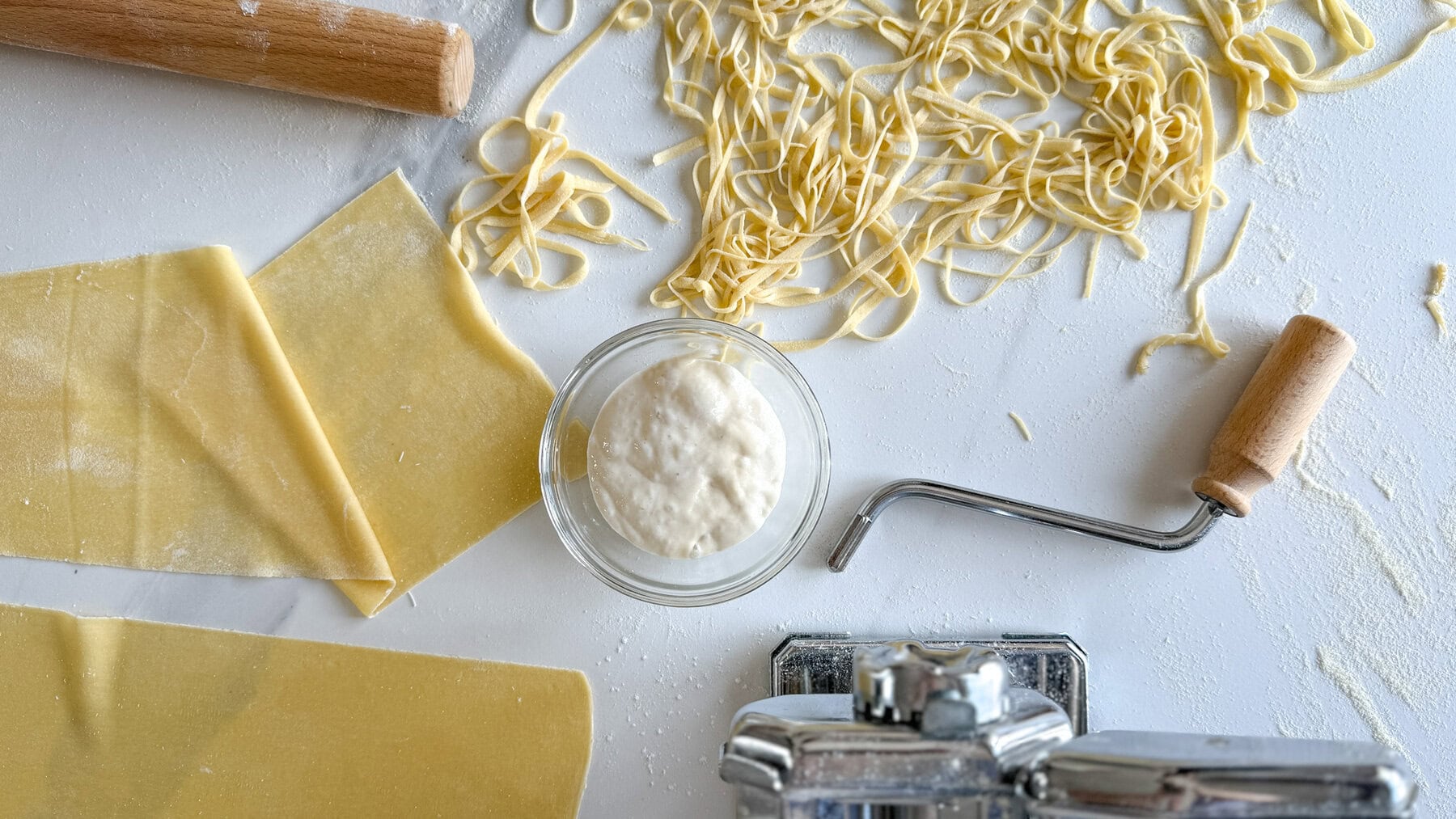 pâtes fraîches maison, bol de levain, machine à pâtes et rouleau à pâtisserie sur comptoir blanc