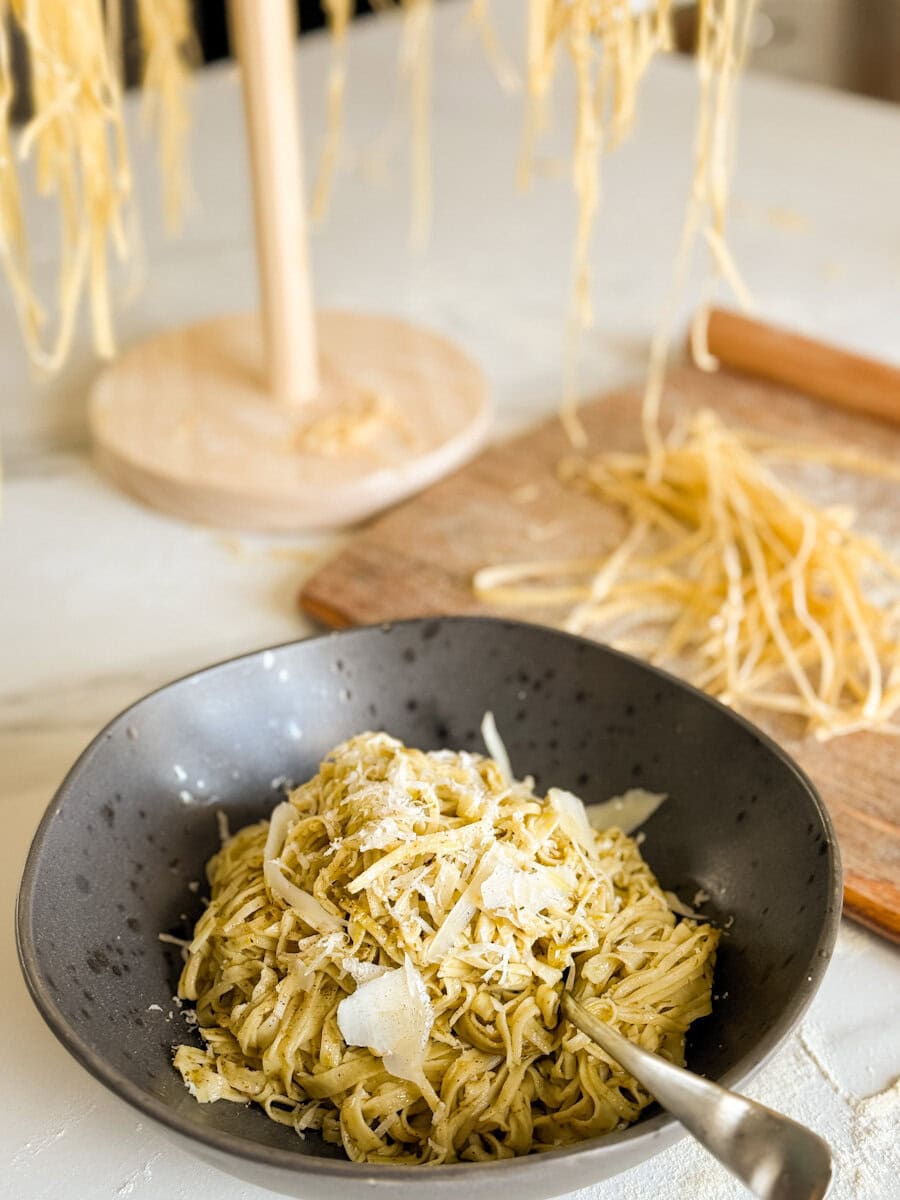bol de pâtes au pesto avec pâtes fraiches qui sèchent derriere sur support et planche en bois