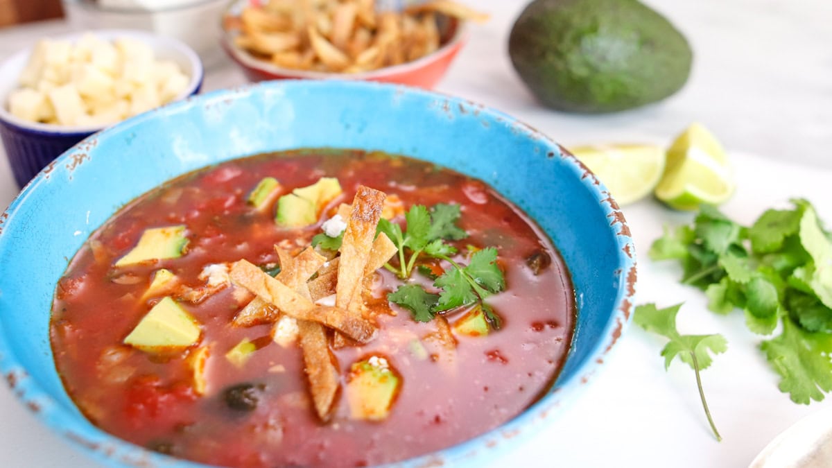 sopa de tortilla dans un bol bleu avec avocat et lanières de tortilla en arrière plan