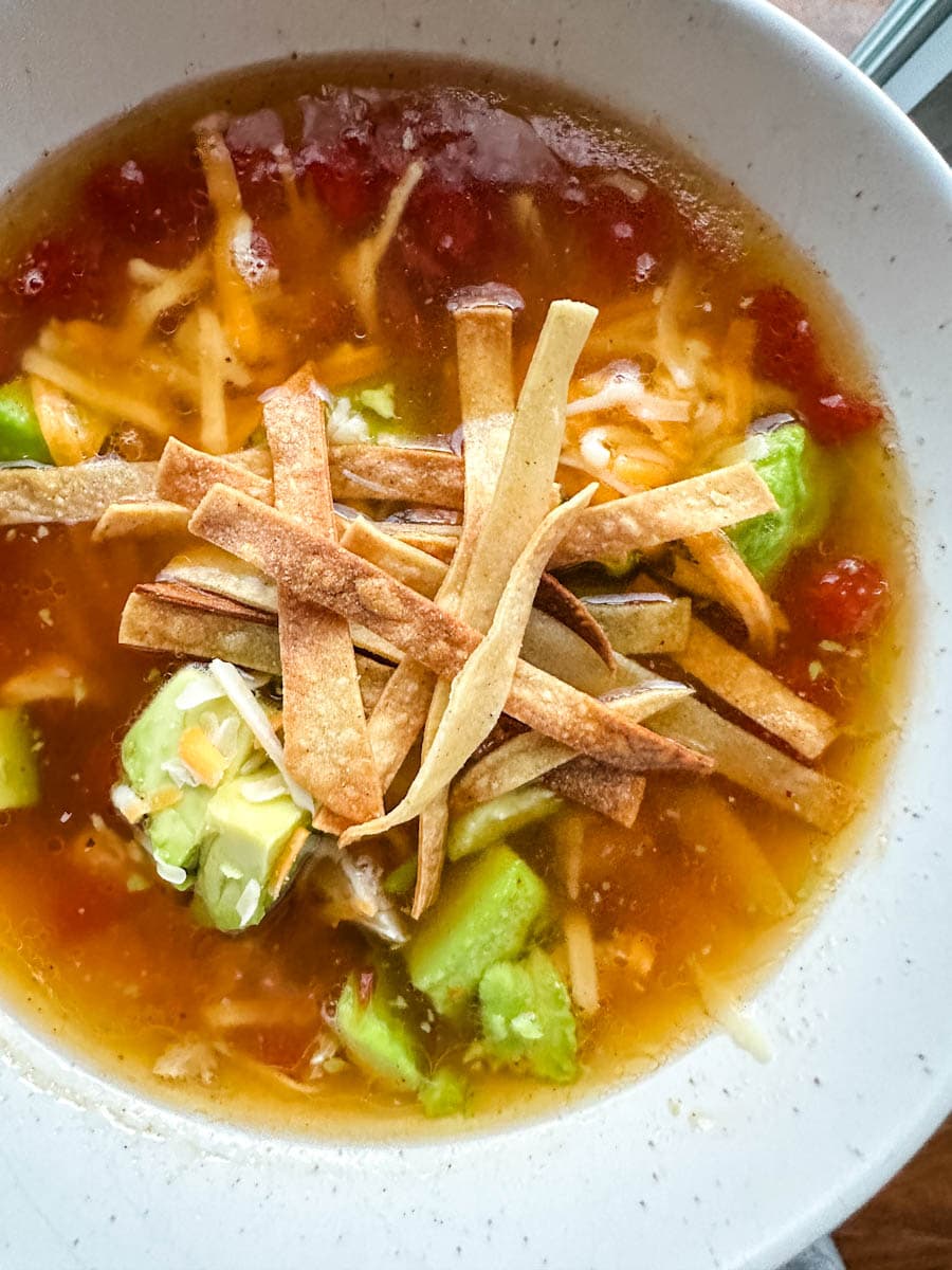 vue rapprochée dans un bol de soupe aux tortillas (sopa de tortilla) garnie de fromage, avocat, coriandre et lanières de tortilla dans un bouillon rouge et riche