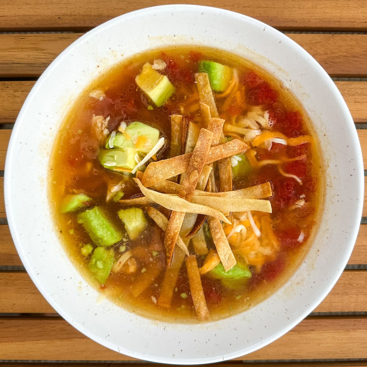 bol de soupe sopa de tortilla dans un bol blanc avec avocat, fromage, tortillas en lanière sur une table en bois