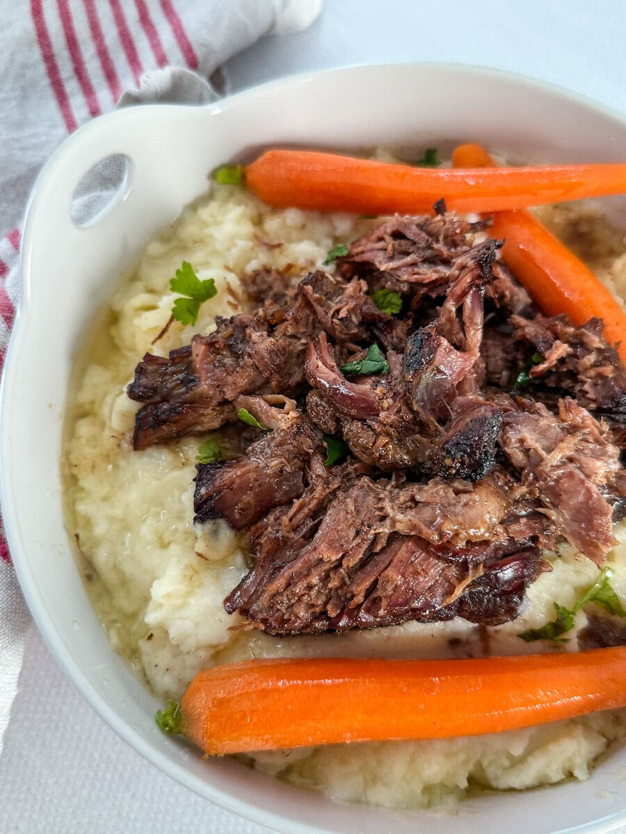 palette de boeuf effilochée avec carottes sur purée de pomme de terre et jus de cuisson dans un plat blanc