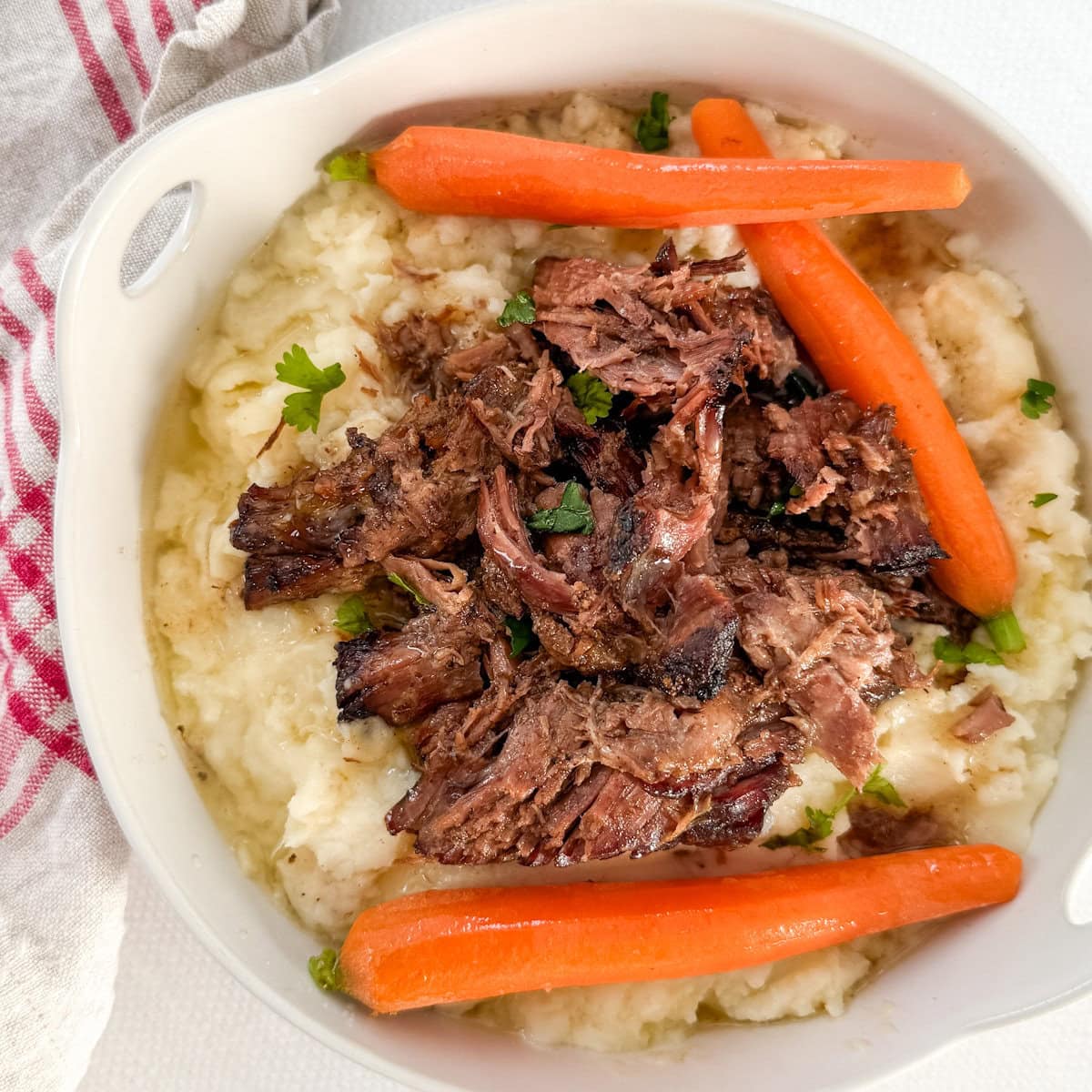 palette de boeuf effiloché avec carottes sur purée de pomme de terre dans un plat rond blanc
