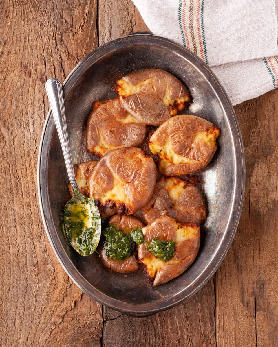 Patates grillées et écrasées dans un plat ovale avec une sauce verte dans une cuillère