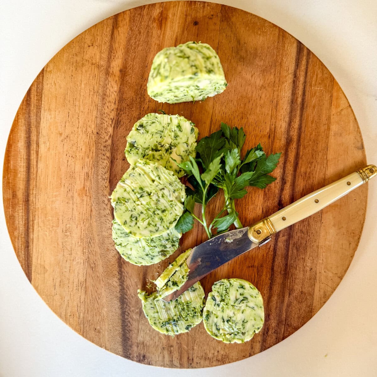 beurre à l'ail en rondelles sur une planche en bois avec petit couteau et feuilles de persil