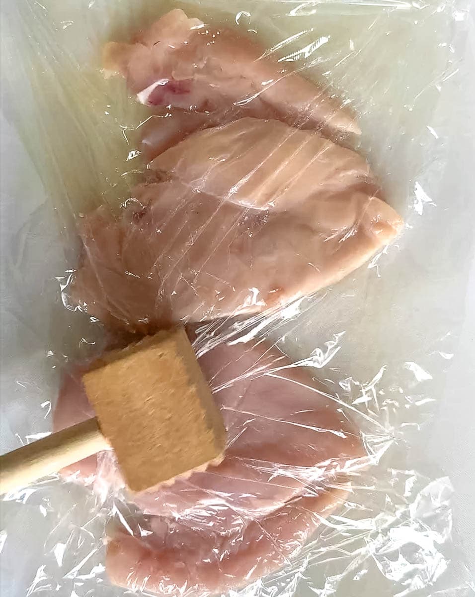 maillet de bois qui applati des poitrines de poulet entre pellicules de plastique