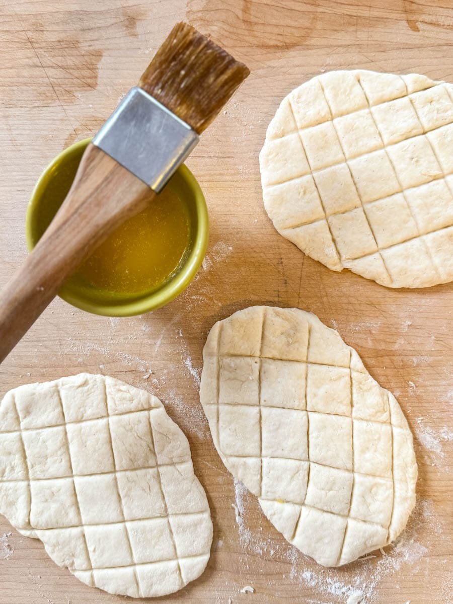 trois queues de castor non cuites sur plan de travail en bois avec petit bol de beurre fondu et pinceau