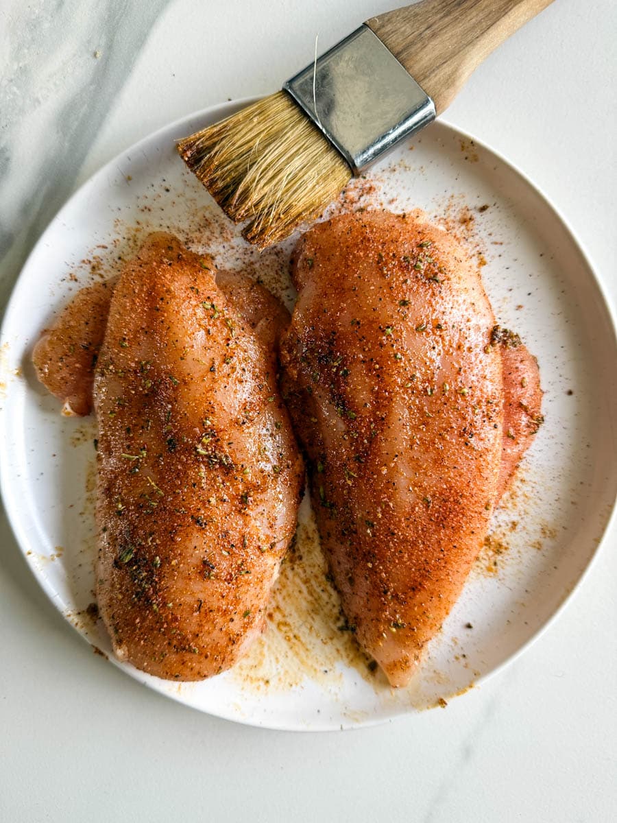 deux poitrines de poulet crues et assaisonnées dans une assiette blanche