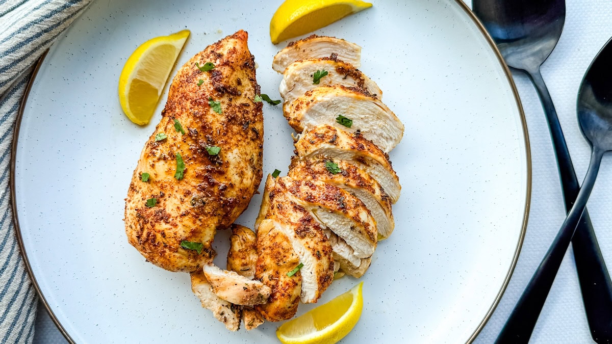 deux poitrines de poulet grillées dans une assiette blanche avec quartiers de citron