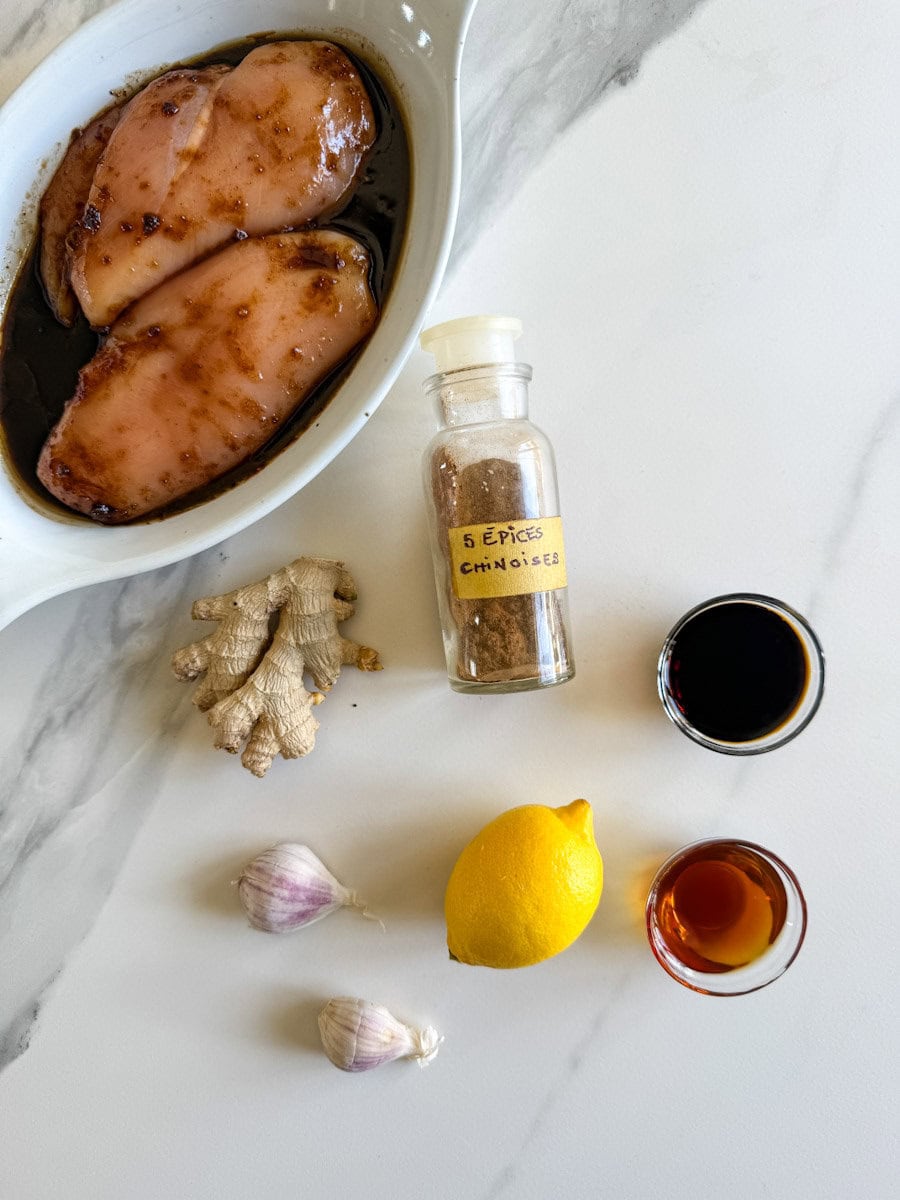poitrines de poulet en marinade, 5 épices chinoises, gingembre, citron, ail et petits bols de sauce sur comptoir blanc