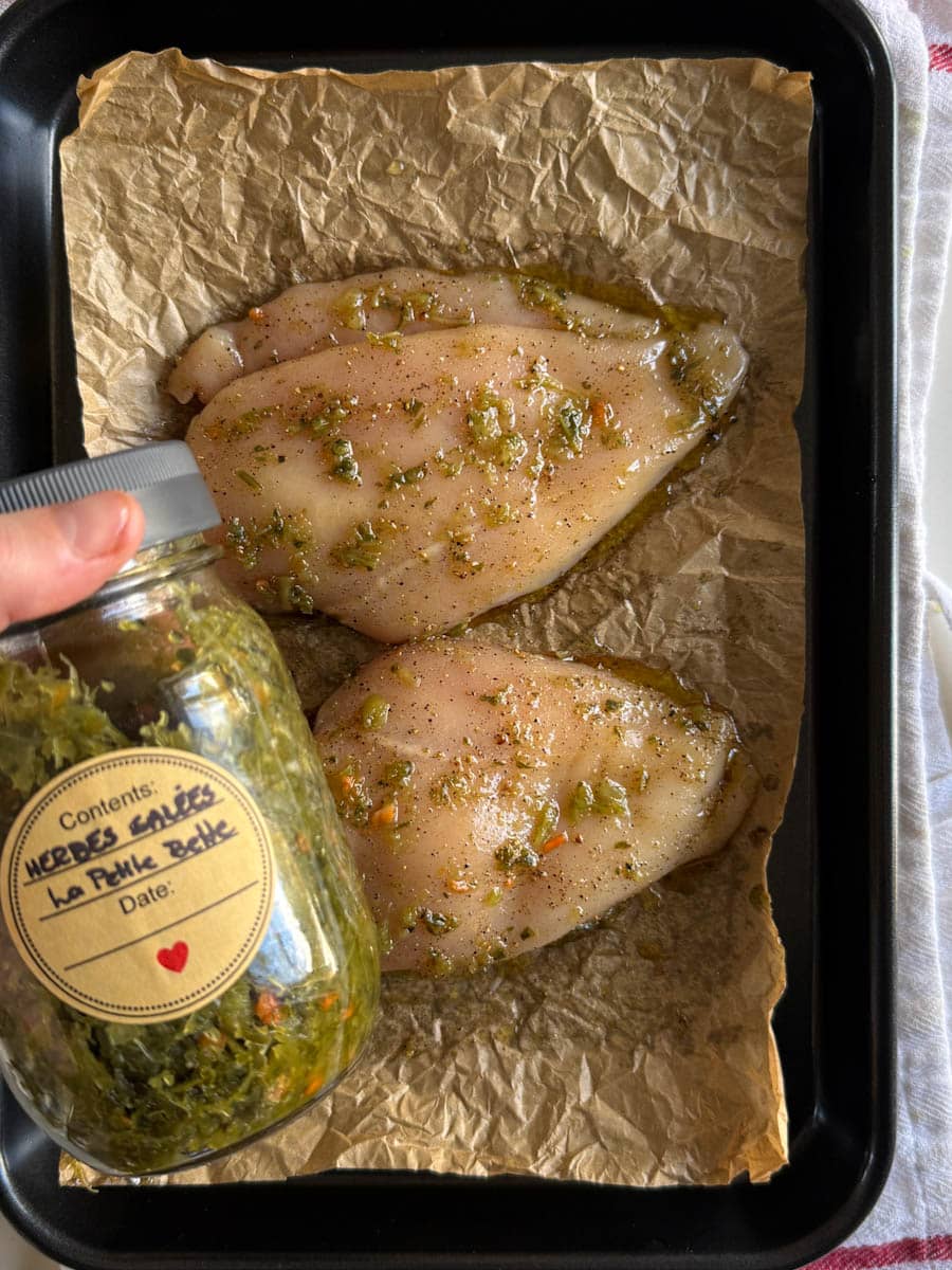 main qui tient le pot d'herbes salées devant poitrines assaisonnées non cuites sur une plaque