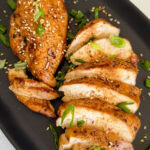 poitrines de poulets grillées à l'asiatique dans une assiette ovale noire avec oignons verts hachés et graines de sésame