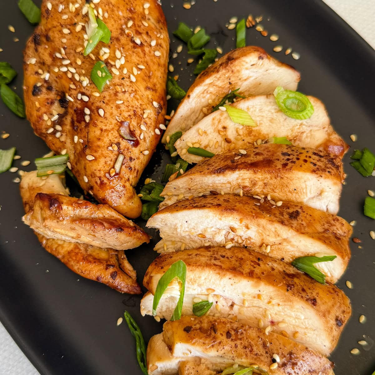 poitrines de poulets grillées à l'asiatique dans une assiette ovale noire avec oignons verts hachés et graines de sésame