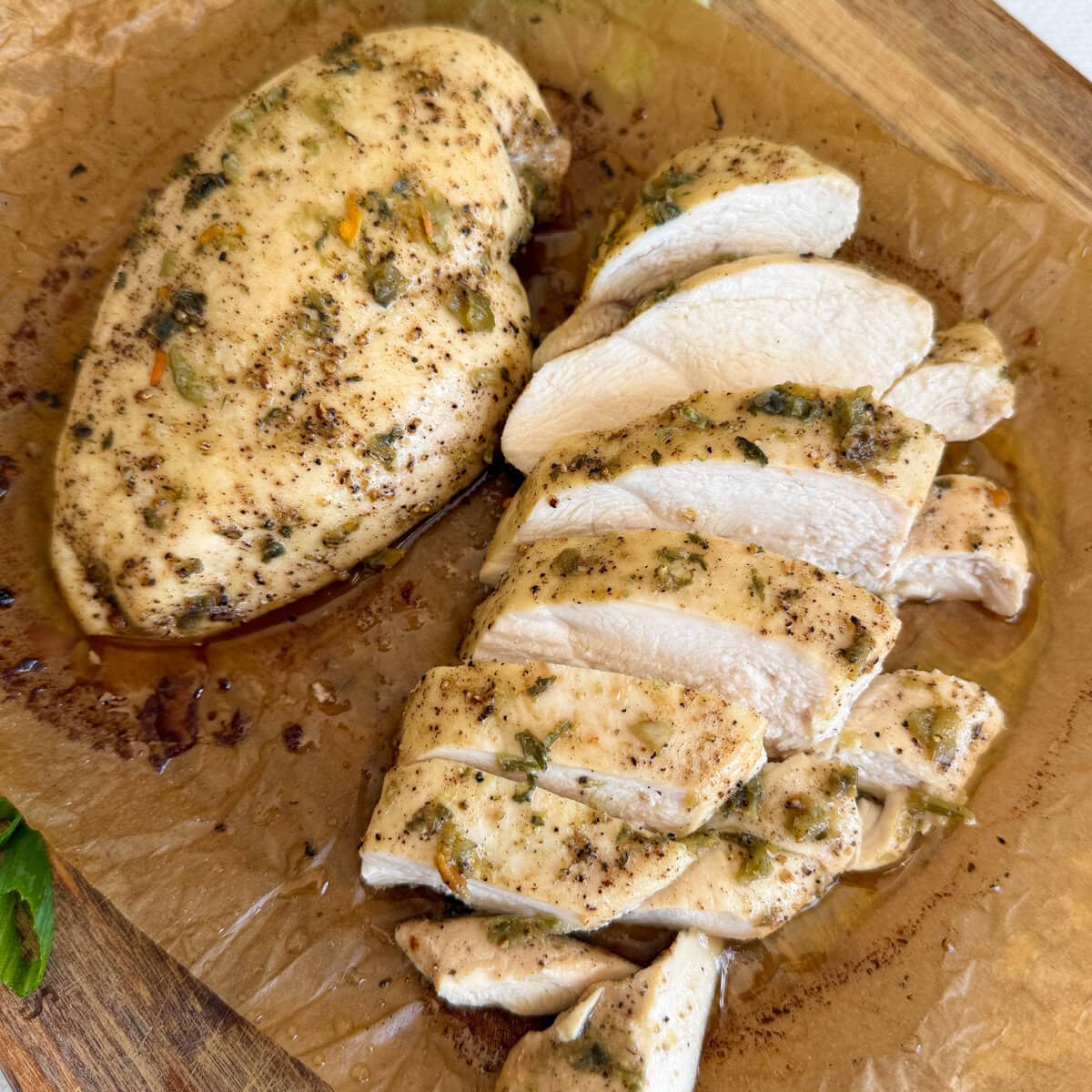 deux poitrines de poulet aux herbes, une coupée en tranches bien juteuses sur papier cuisson