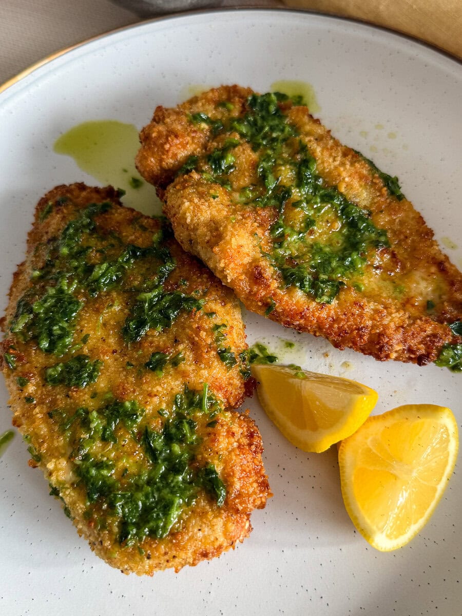 2 escalopes de poulet panées au beurre à l'ail dans une assiette pâle avec quartiers de citron