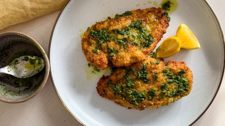 2 escalopes de poulet panées au beurre à l'ail dans une assiette pâte avec quartiers de citron et bol de beurre à l'ail avec cuillère