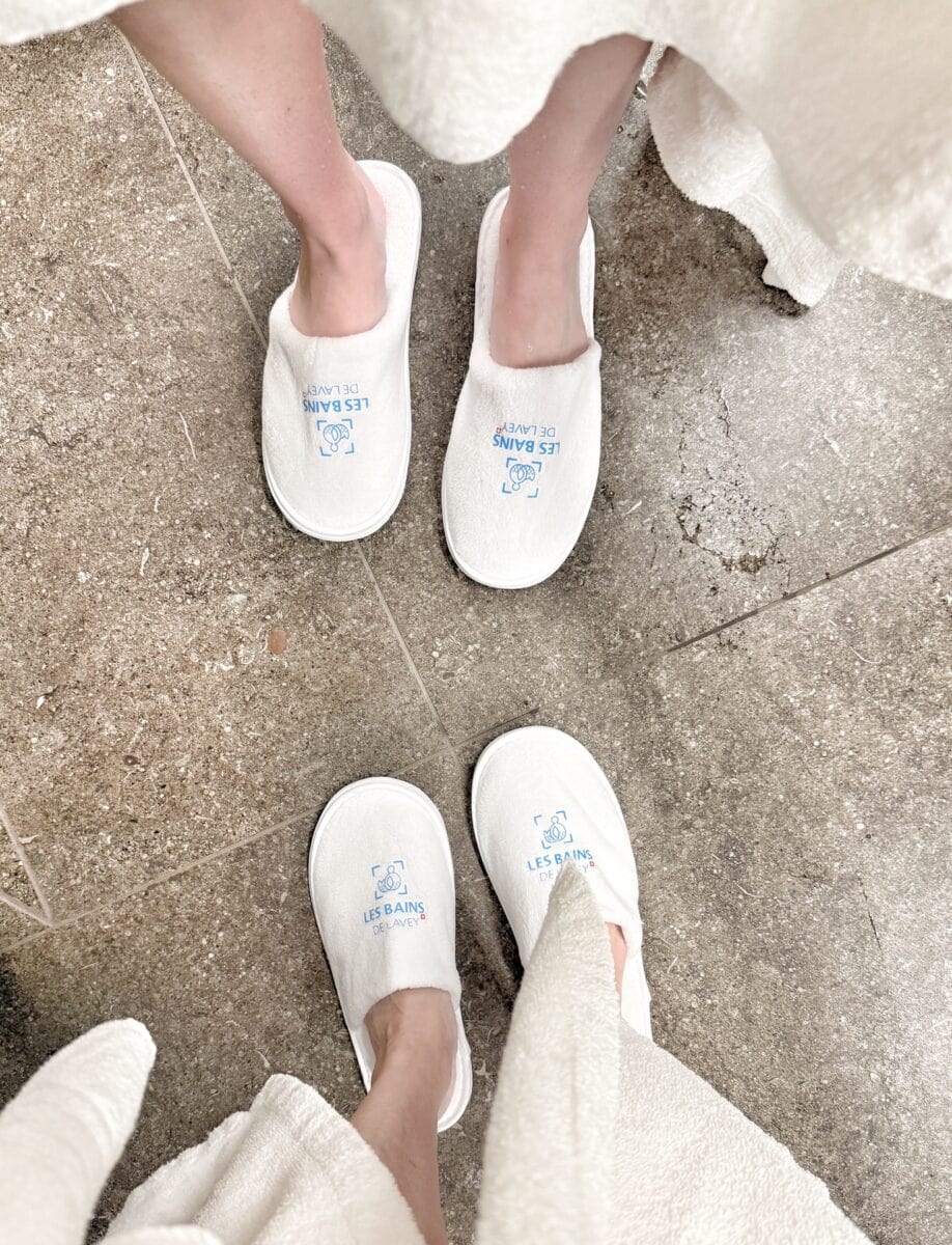 deux pieds en pantoufle et bas de peignoir blanc avec "bains de Lavey" écrit sur pied
