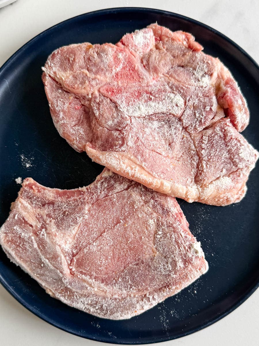 2 côtelettes de porc enrobées de farine dans une assiette bleu foncé