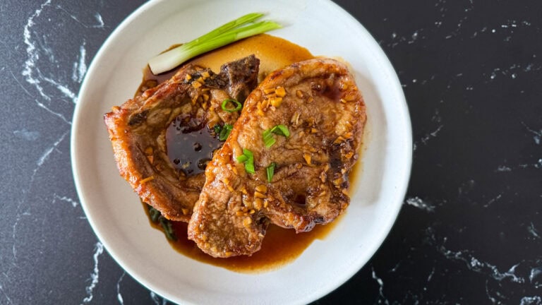 2 cotelettes de porc en sauce sucrée avec oignons verts dans un bol sur comptoir noir marbré