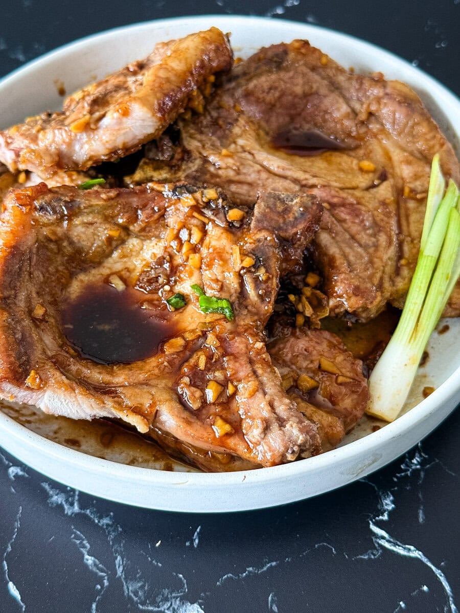 4 cotelettes de porc en sauce sucrée chinoise dans une assiette blanche avec oignon vert