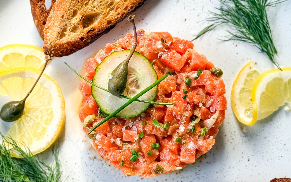 tartare de saumon dans une assiette avec citron, aneth et croûtons
