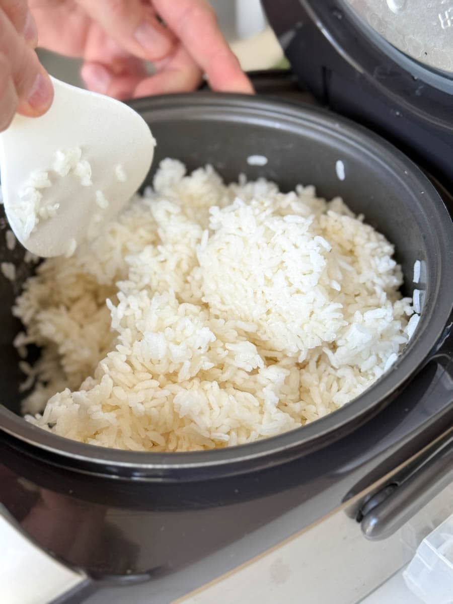 main qui brasse le riz à sushi dans un bol de machine à riz