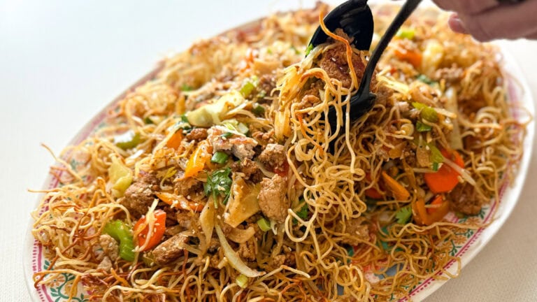 grand plat ovale de chow mein sur nouilles frites avec mains qui servent une portion avec cuillères de service