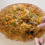 mains qui sert du chow mein aux légumes et au porc