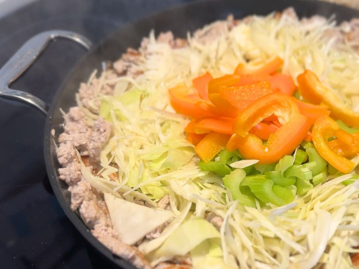 chow mein dans un grand wok ou poêlon en train d'ajouter ingrédients