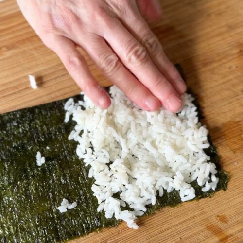 main qui étent le riz dans la feuille d'algue nori pour un sushi cornet