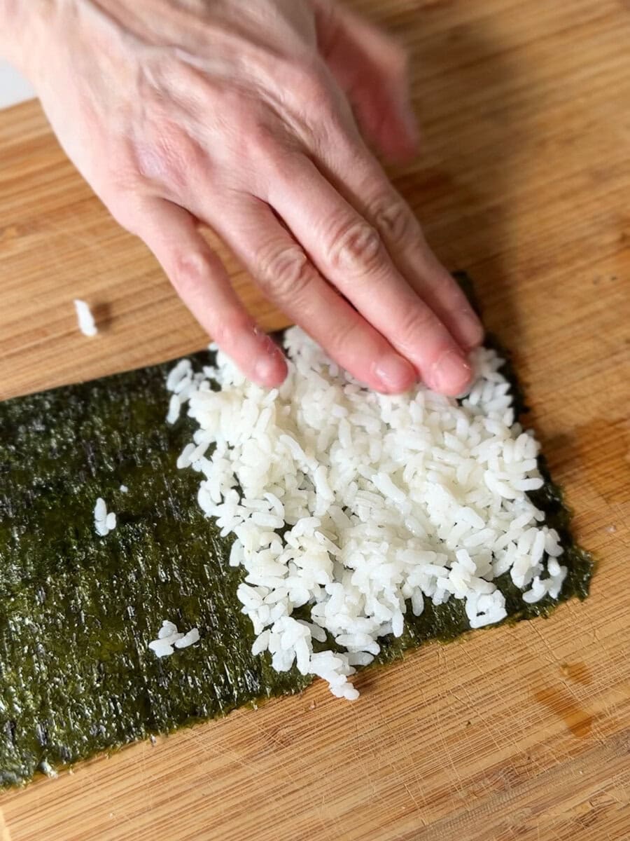 main qui étent le riz dans la feuille d'algue nori pour un sushi cornet
