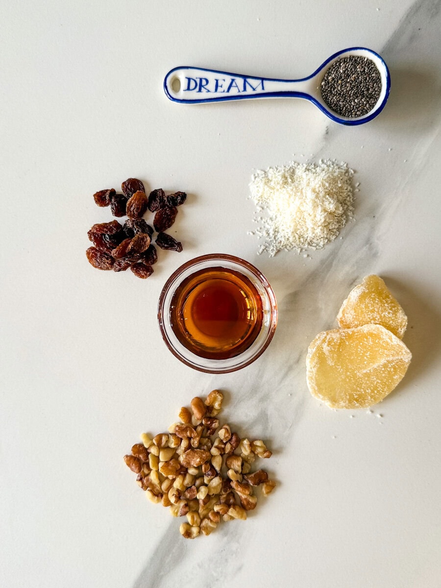 ingrédients sur comptoir blanc: raisins, graines de chia, noix de coco, sirop d'érable. gingembre confit