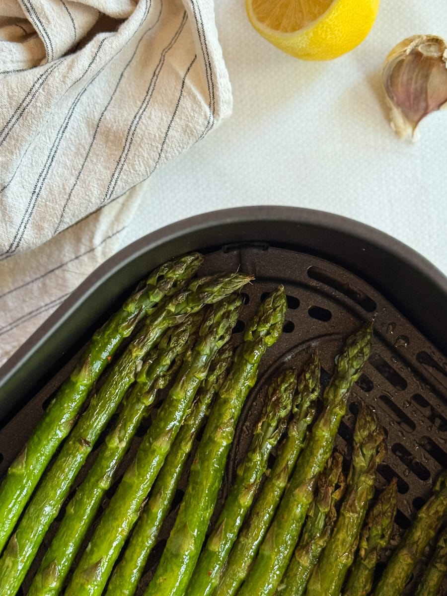 asperges grillées dans le panier du air fryer sur comptoir avec citron, ail et linge de table