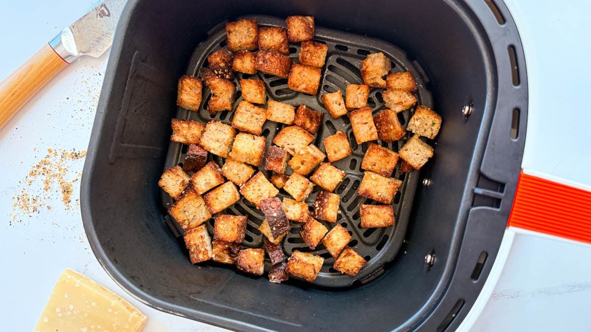 croûtons maison dans le panier du air fryer, fromage, couteau sur comptoir à côté