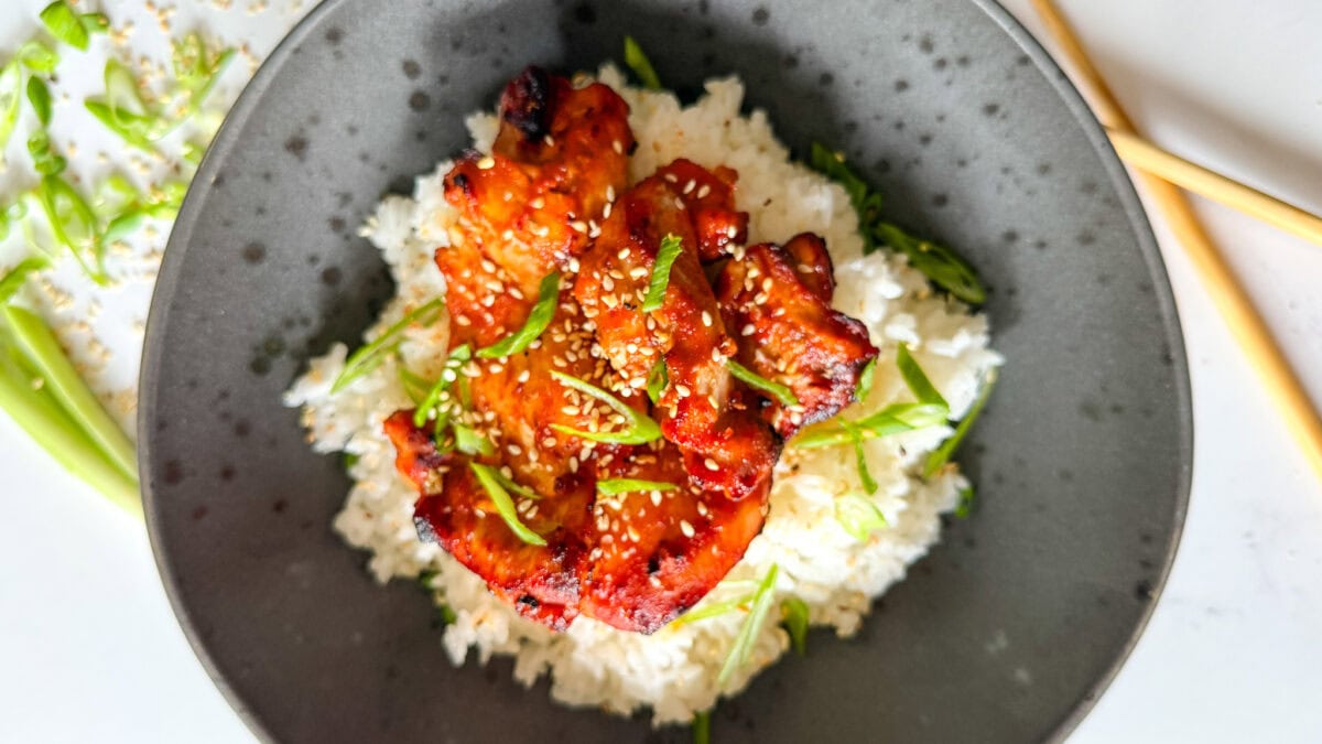 poulet gochujang dans un bol noir avec riz, oignon vert et graines de sésame