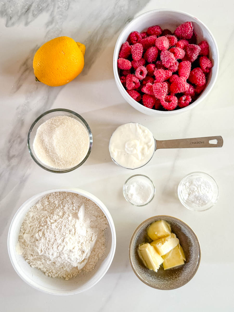 ingrédients pour muffin framboise, citron, sucre, beurre, yogourt, farine sur comptoir blanc marbré