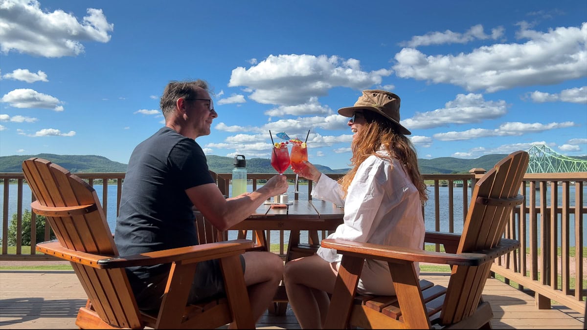 Manon Lapierre et Lionel du Souich qui font cheers avec cocktails vue sur rivière Restigouche et le pont de Campbellton