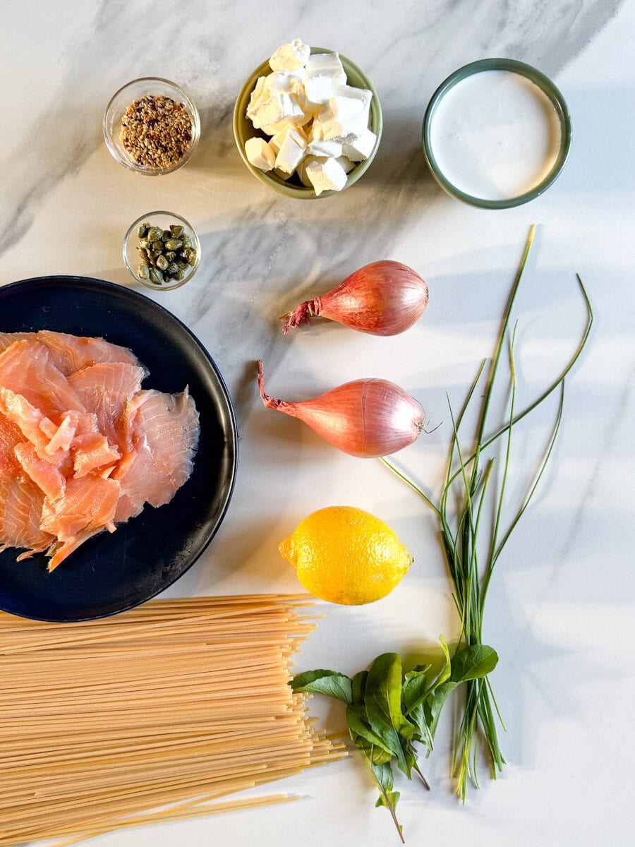 Ingrédients sur comptoir marbré blanc: spaguetti, saumon fumé, échalote, citron, herbes, fromage à la crème, crème