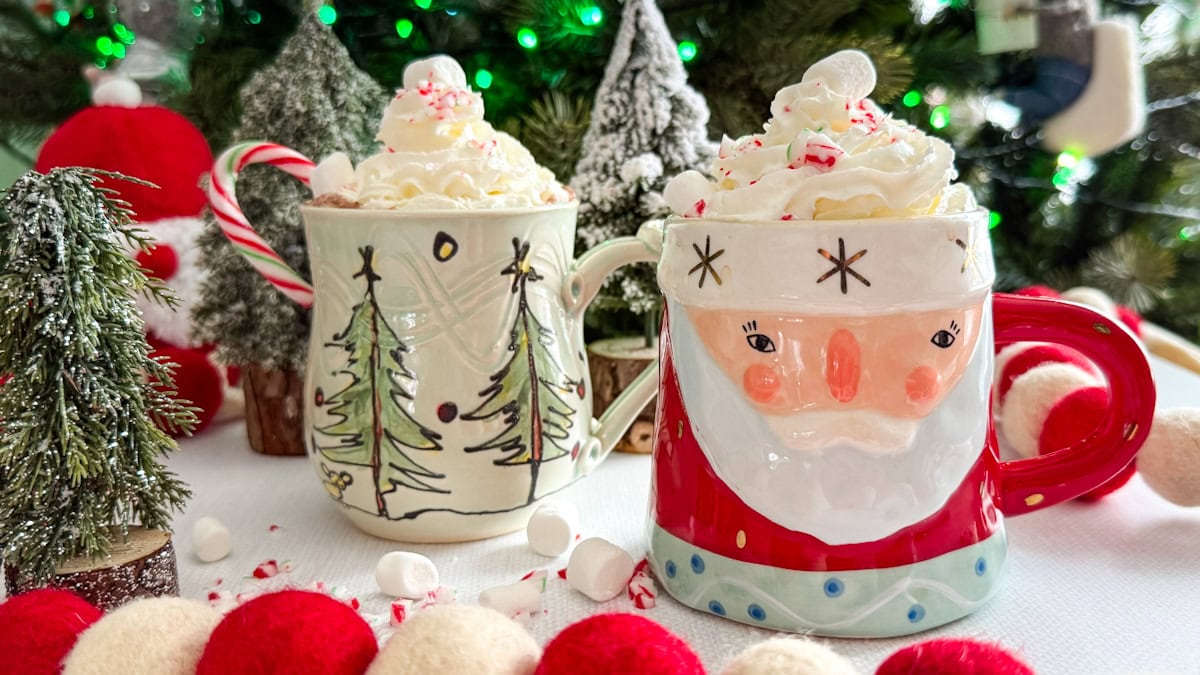 2 tasses de chocolat chaud gourmand avec crème fouettée et guimauves devant décorations de Noël