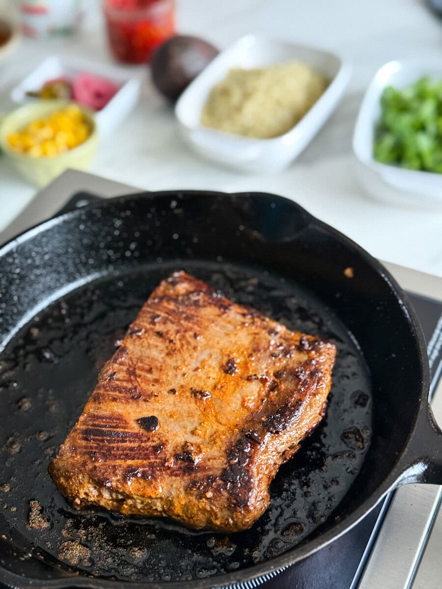 steak chipotle qui grille dans une poêle en fonte devant ingrédients pour bol ou burrito sur comptoir