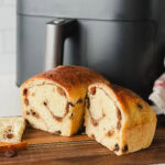 pain aux raisins coupé en deux sur planche de bois devant un air fryer gris foncé