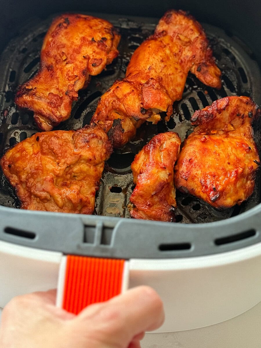 poulet chipotle grillé dans le panier du air fryer, main tenant la poignée